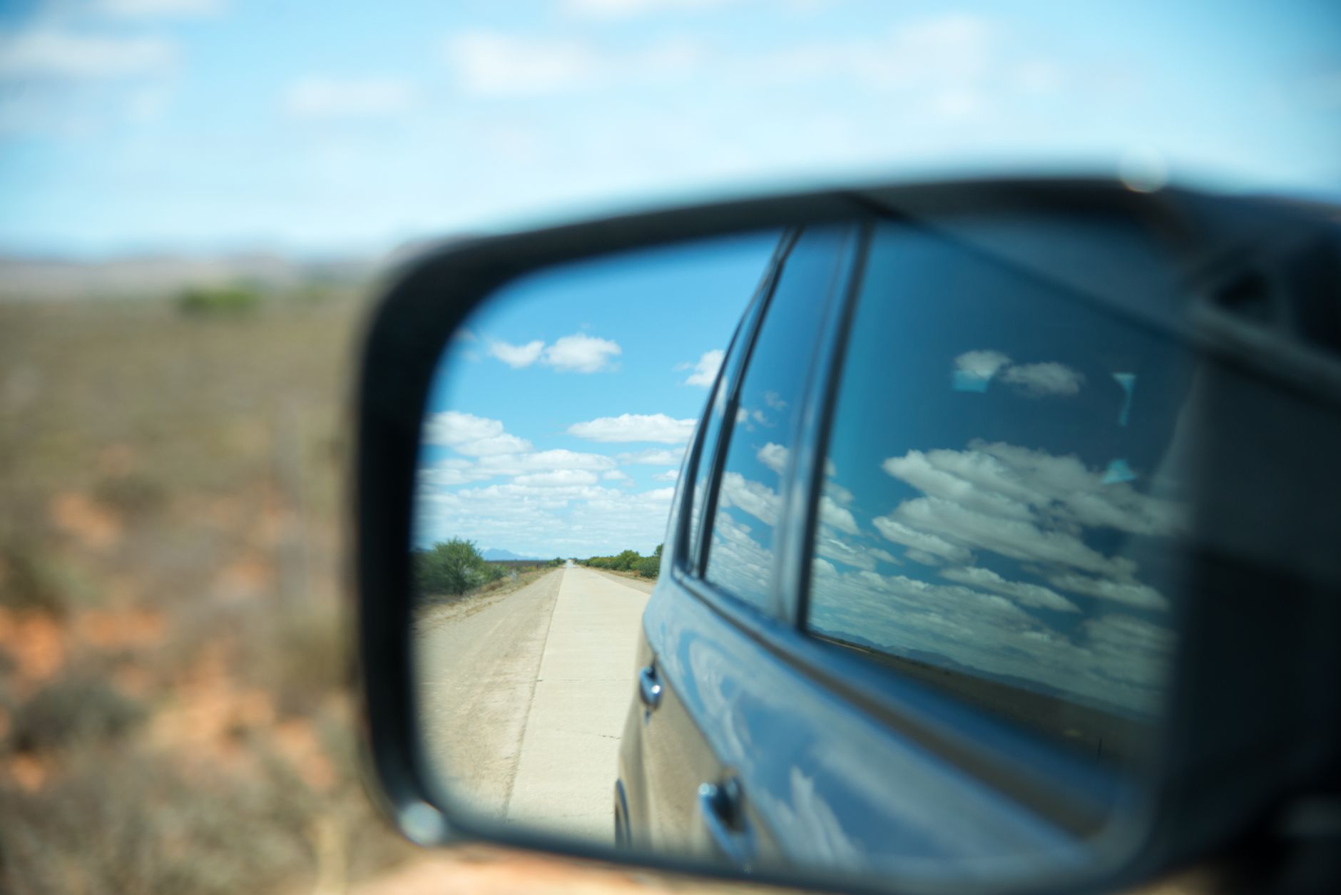 A view of the road behind reflected in a car wing mirror