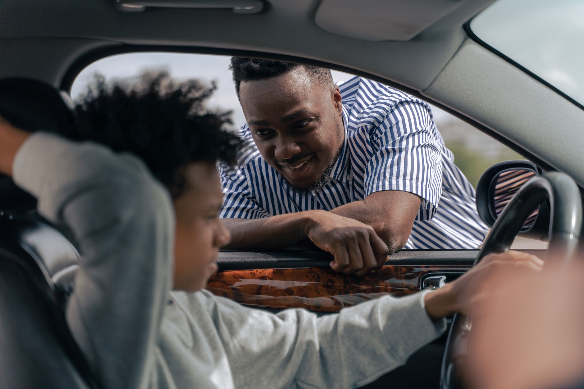 A smiling driving instructor coaching a learner behind the wheel